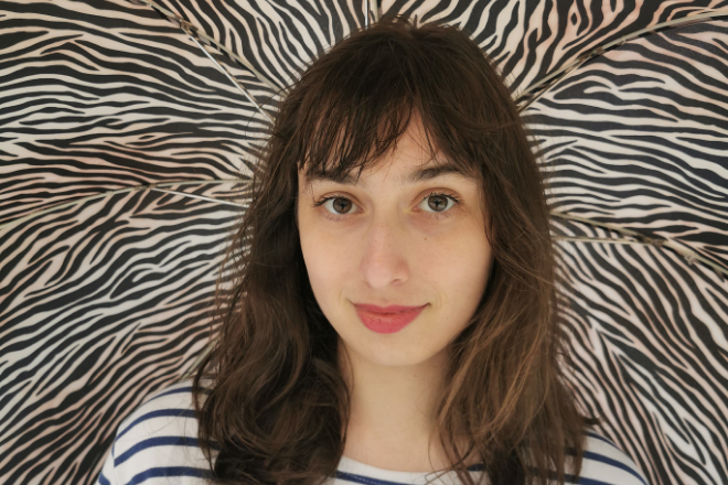 Photographie plan rapprochée de face d'une jeune fille brune avec un fond zébré en arrière-plan.