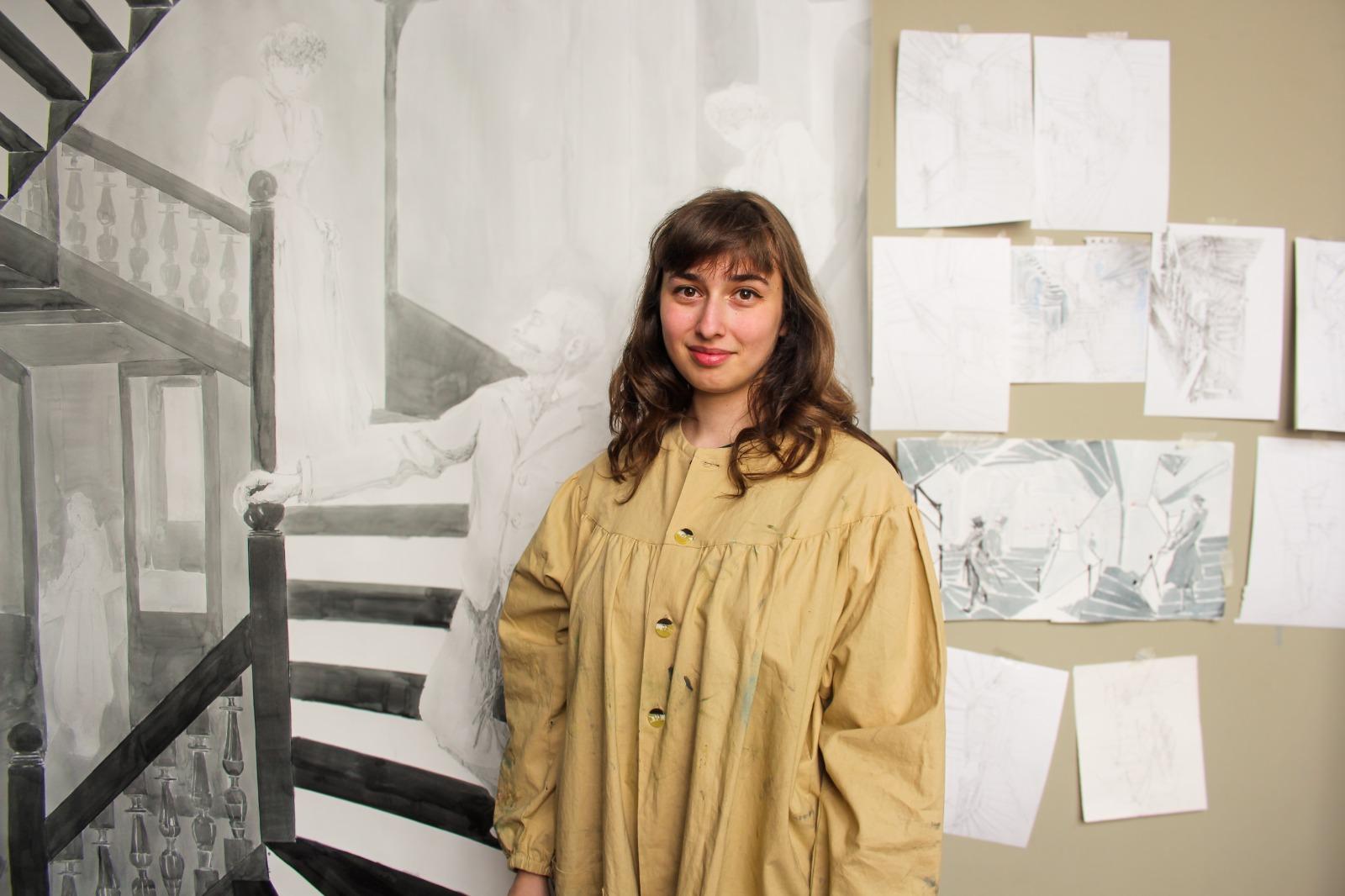 Une femme en blouse d'artiste devant un mur avec des dessins accrochés debout